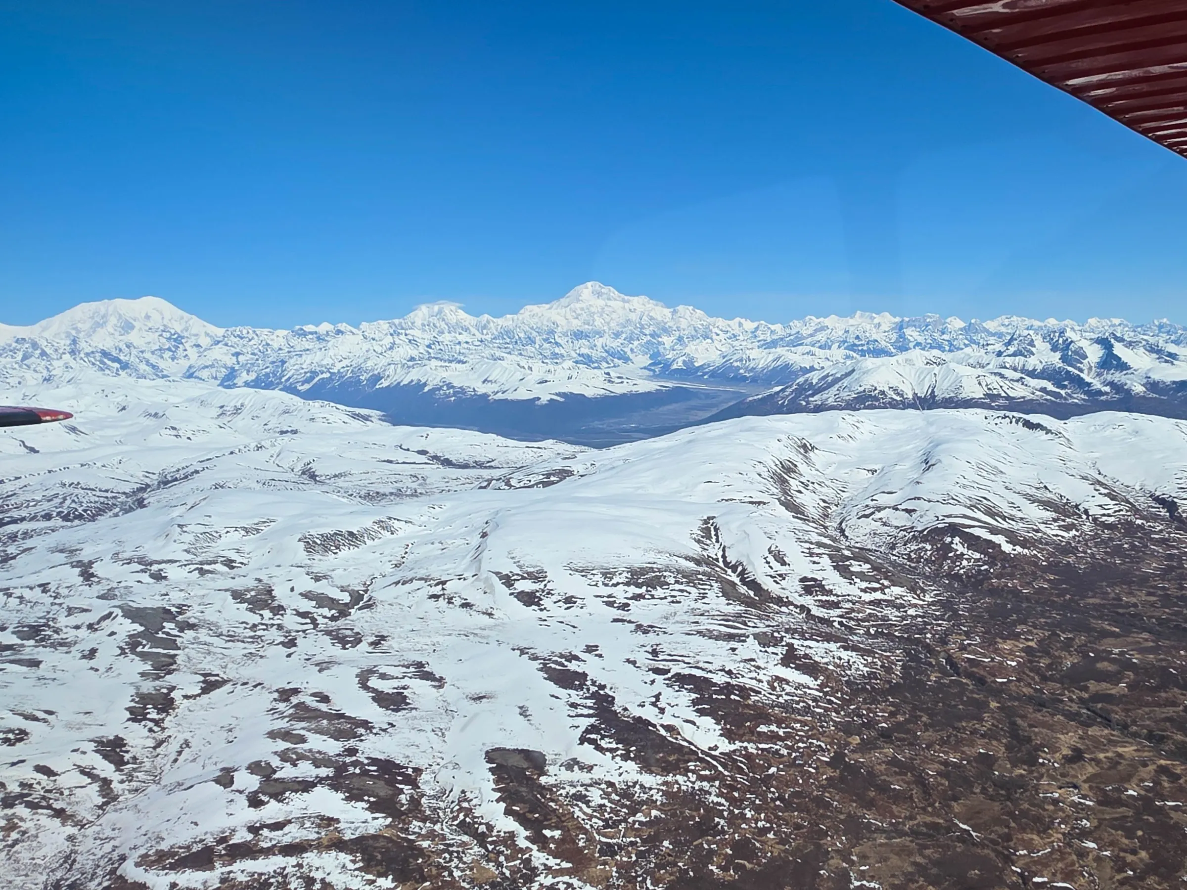 Aerial view of snow-covered mountains under a clear blue sky.