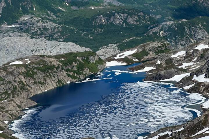 Mountain lake with snow patches and rugged peaks under a cloudy sky.