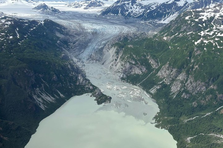 Aerial view of a glacier flowing into a lake surrounded by mountains.