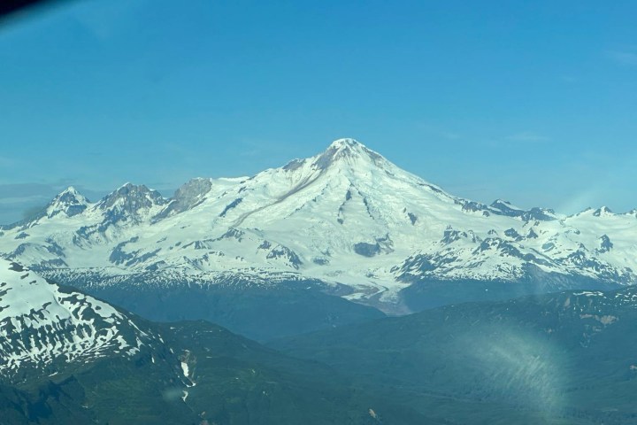 Snow-capped mountain peak under clear blue sky, surrounded by smaller peaks.
