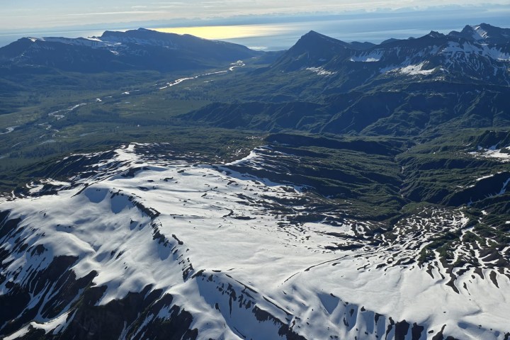 Aerial view of snow-covered mountains under a red plane wing.