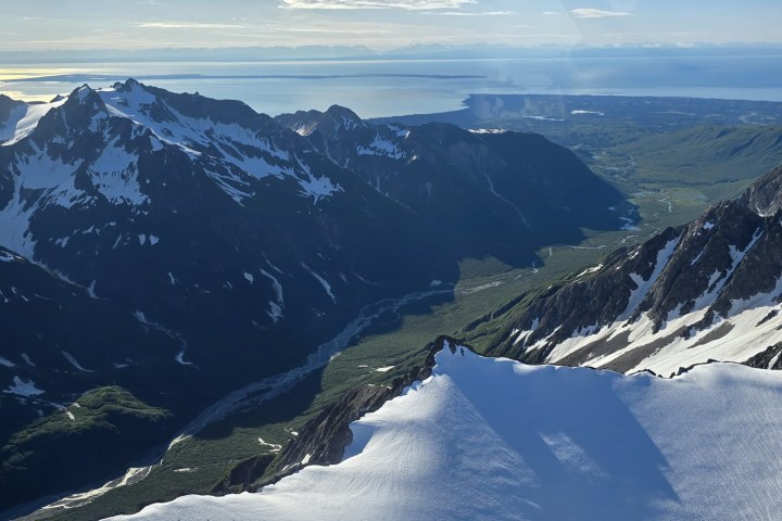 Aerial view of snowy mountains and coastline under plane wing.