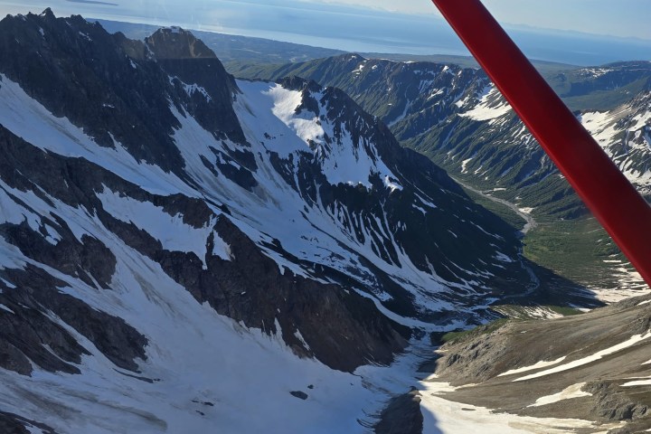 Aerial view of snow-covered mountains and valleys under a red airplane wing.