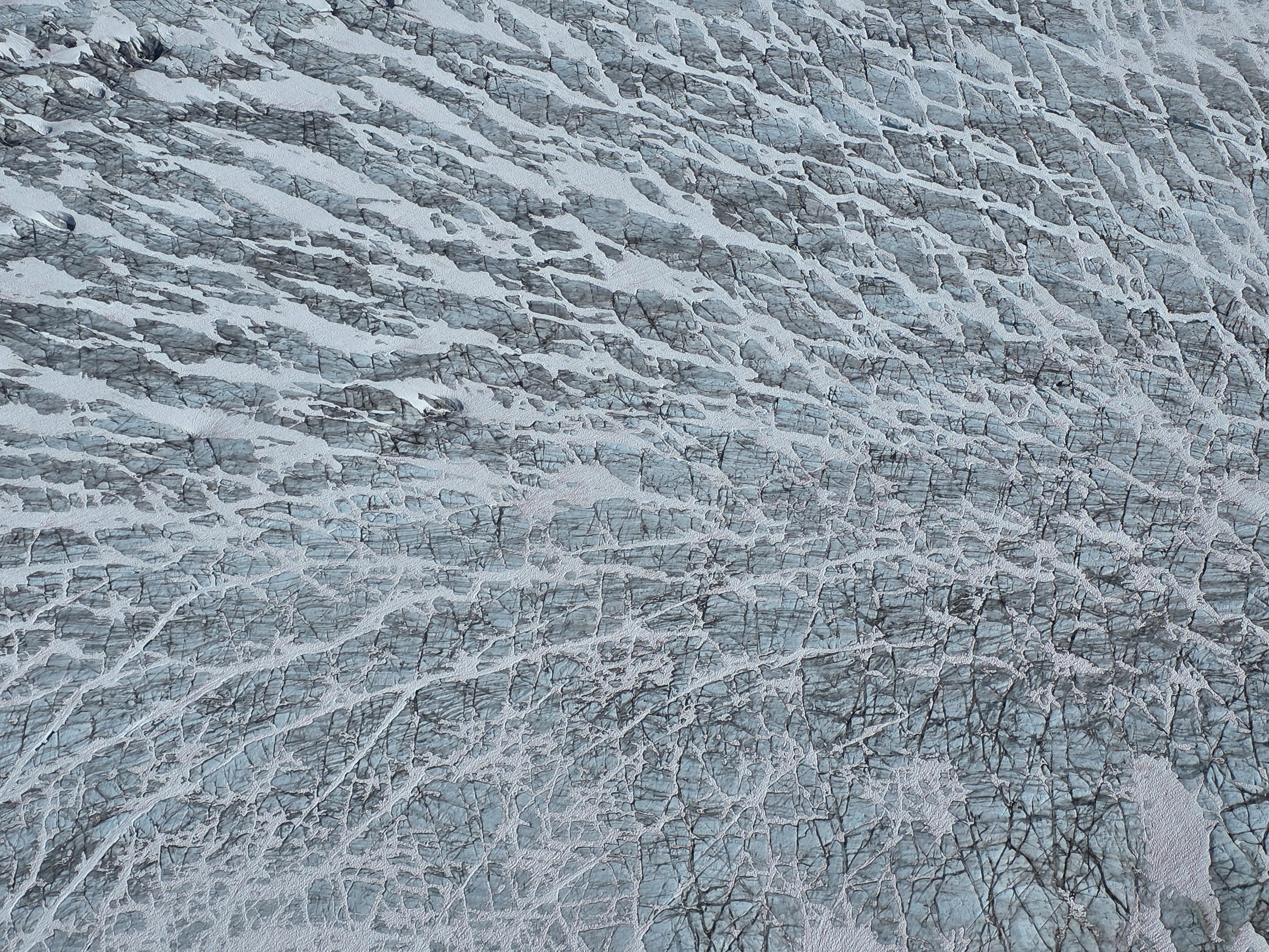 Aerial view of a glacier's cracked, icy surface with patterns of crevices and ridges.