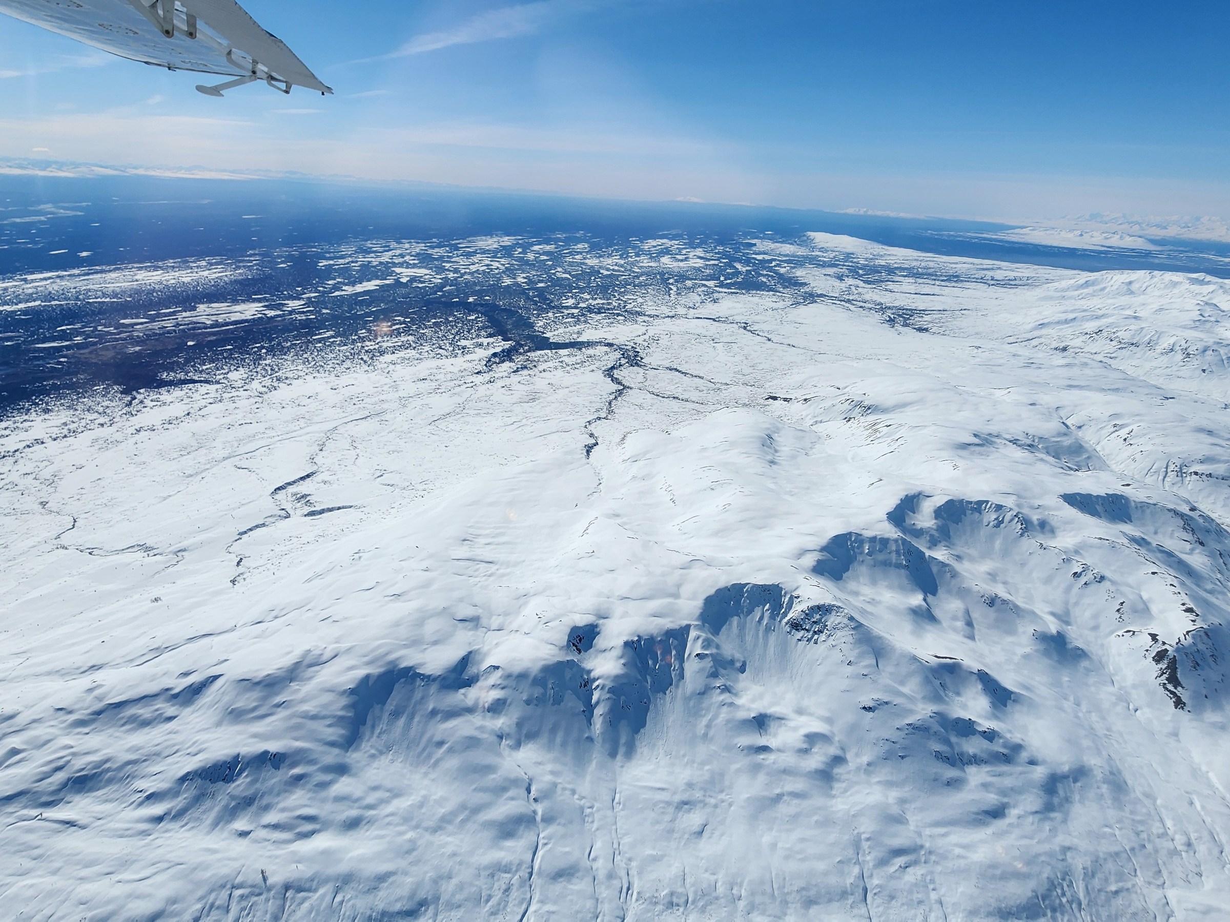 Aerial view of snowy mountains and vast icy landscape under a clear blue sky.