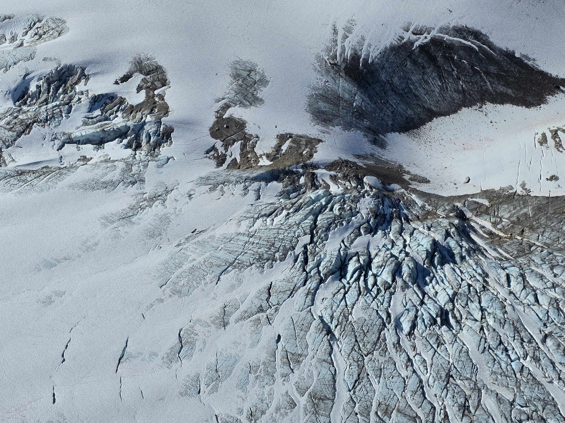 Aerial view of a glacier with crevasses and rocky terrain.