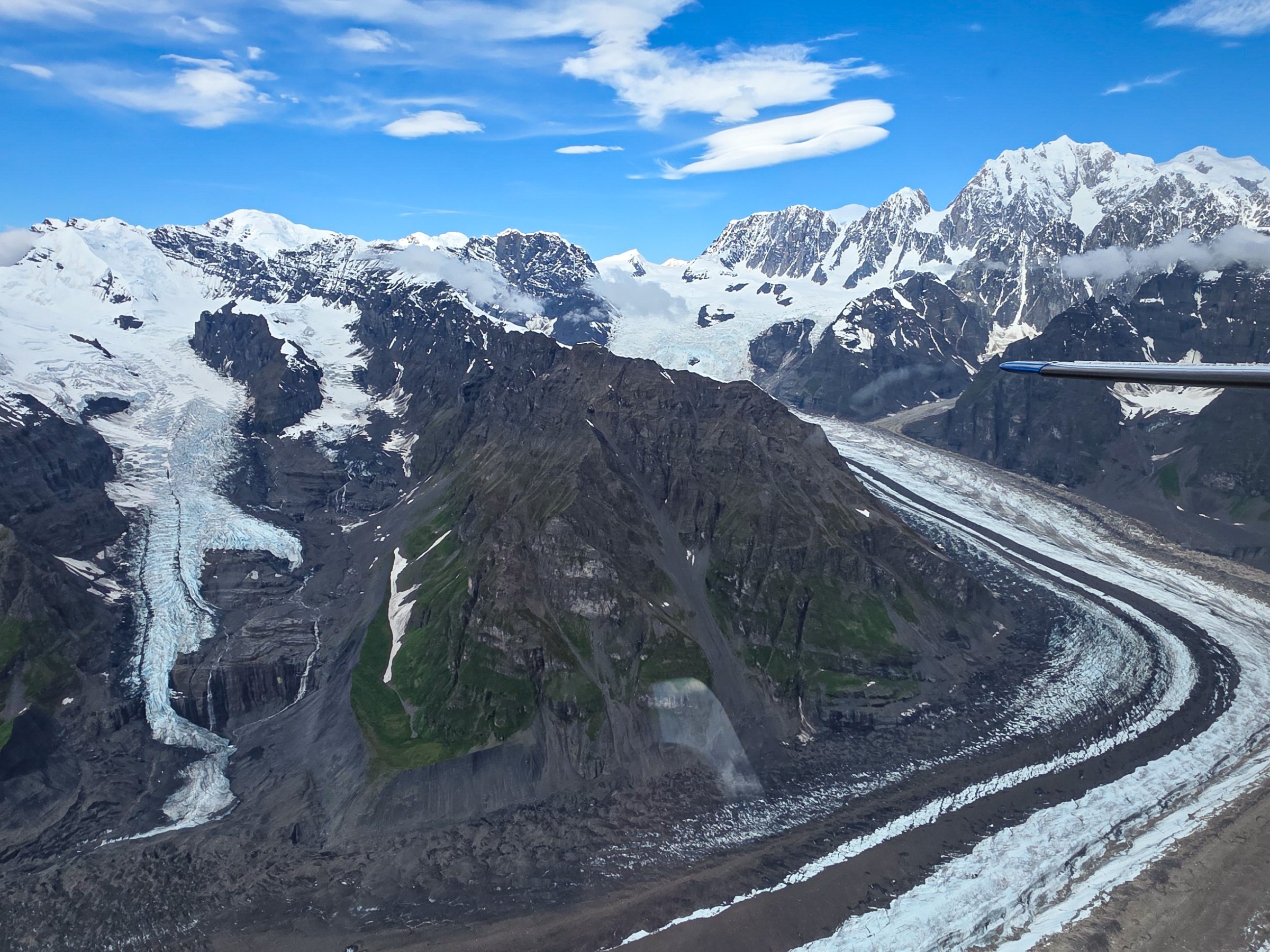 Aerial view of snowy mountains with glaciers under a clear blue sky.