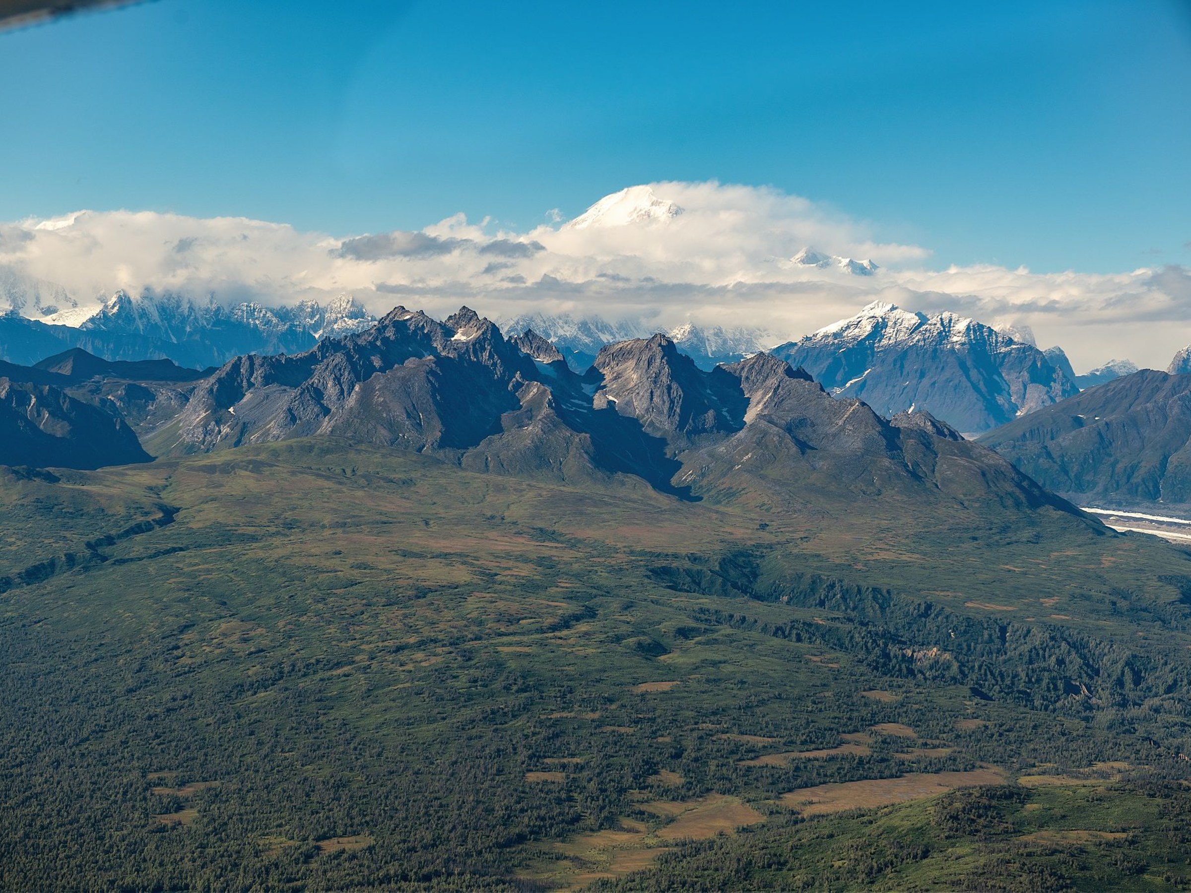 Aerial view of a mountain range with green valleys under a blue sky with scattered clouds.