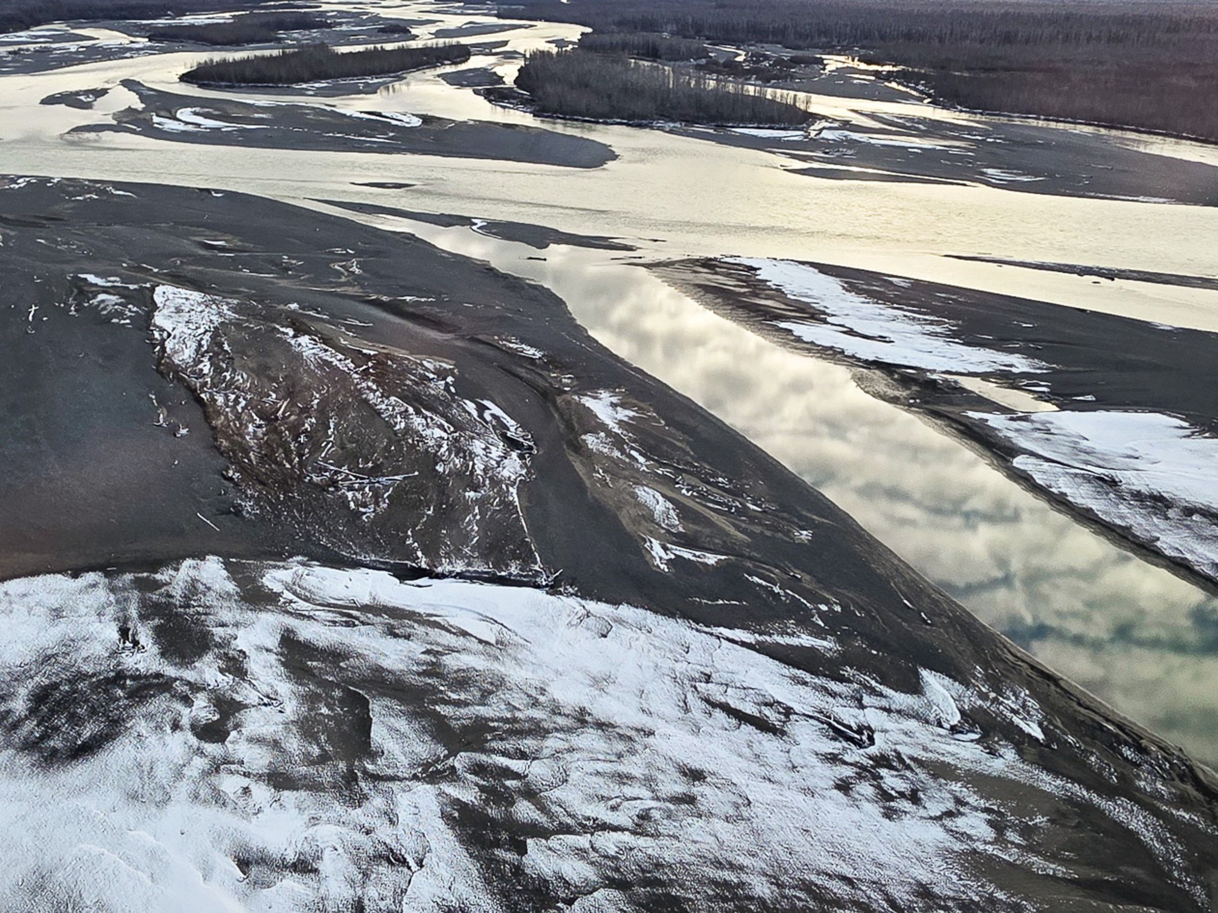 Aerial view of a river with sandbanks and patches of snow.